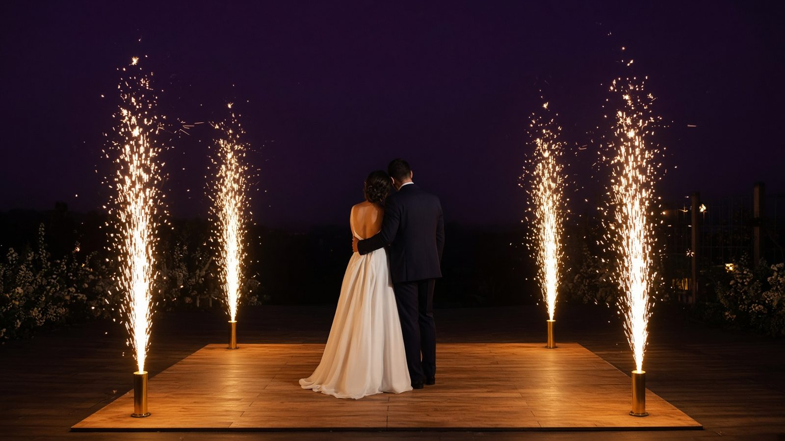 A bride and groom on a dance floor with four gold cold-spark fountains at the corners.