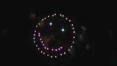 A fireworks shell broken into a smiley of white sparks with a purple smile against a black sky.